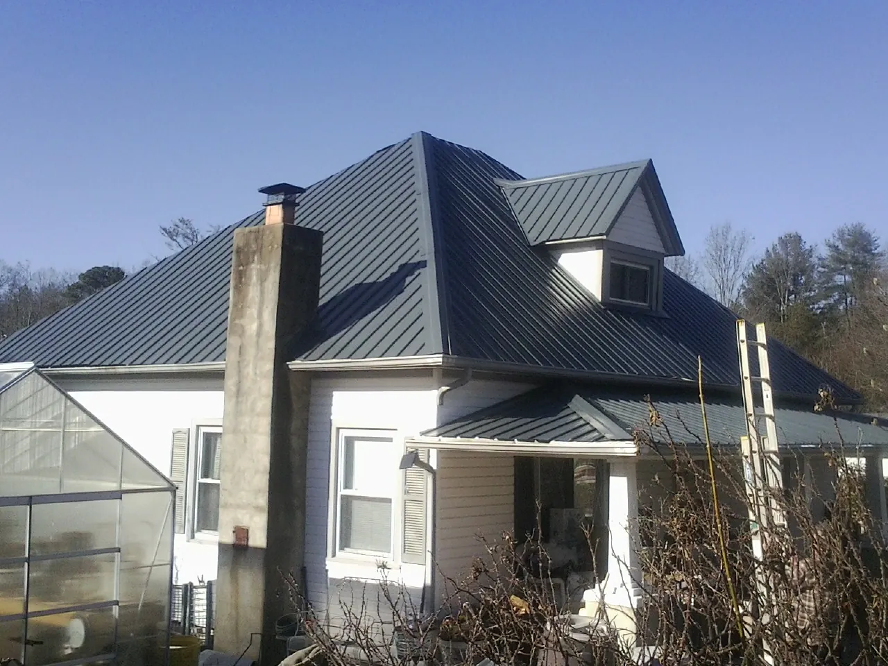 Dark blue standing seam metal roof on a white farmhouse with dormer — Slate & Tile Roof Repair by Roofing Brothers in Bedrock