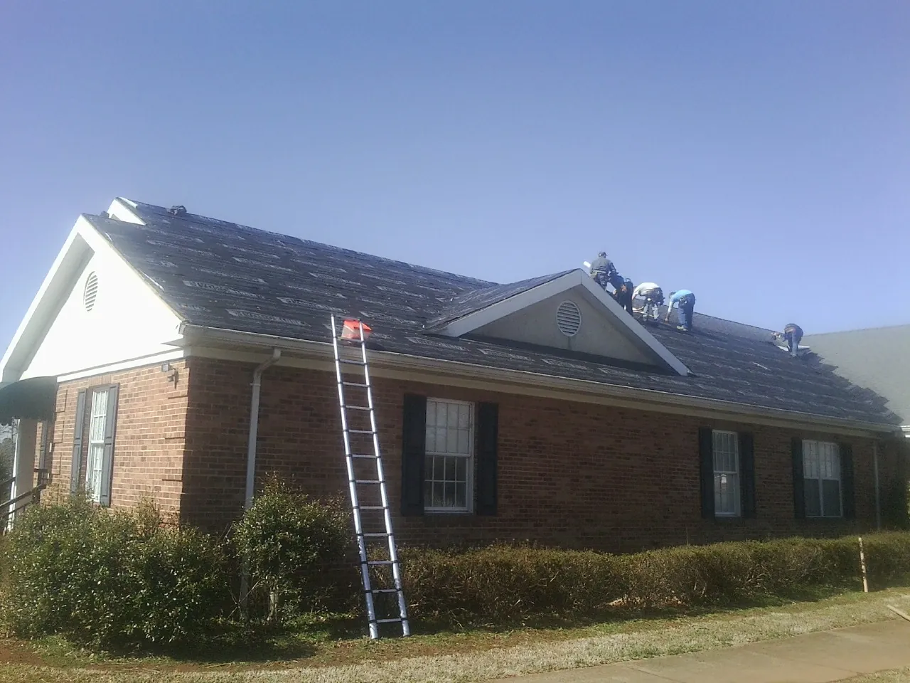 Crew tearing shingles off a brick ranch roof with a ladder set — Emergency Roof Repair work by our crew in Bedrock