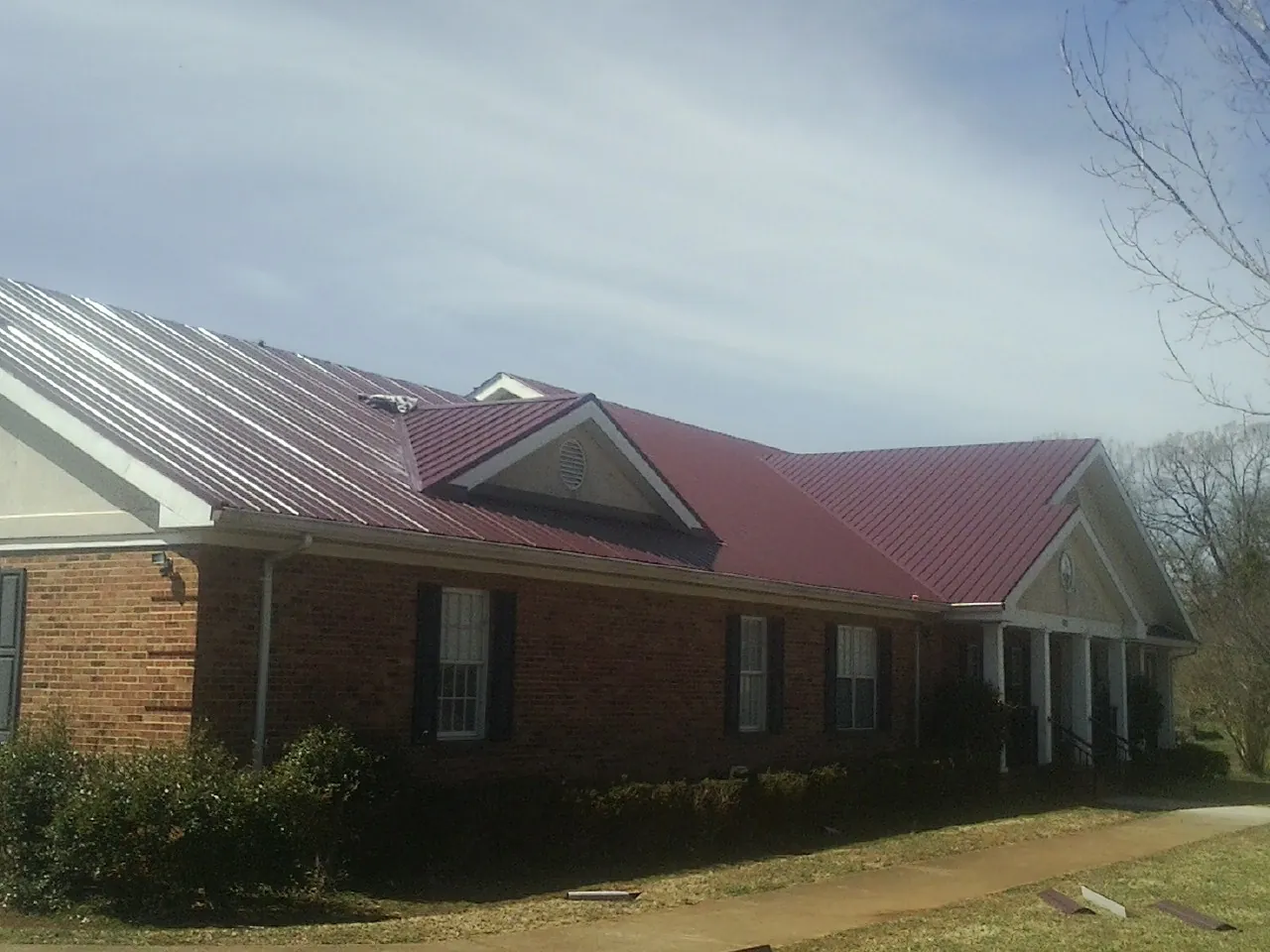 Red metal roof with gabled entries on a long brick building, from a Hail Damage Roof Repair job in Bedrock