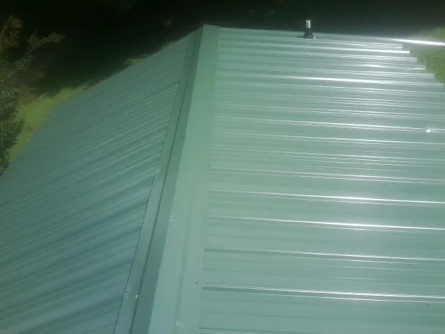 New green metal panels meeting at the ridge of a roof — Flat Roof Repair work by our crew in Bedrock