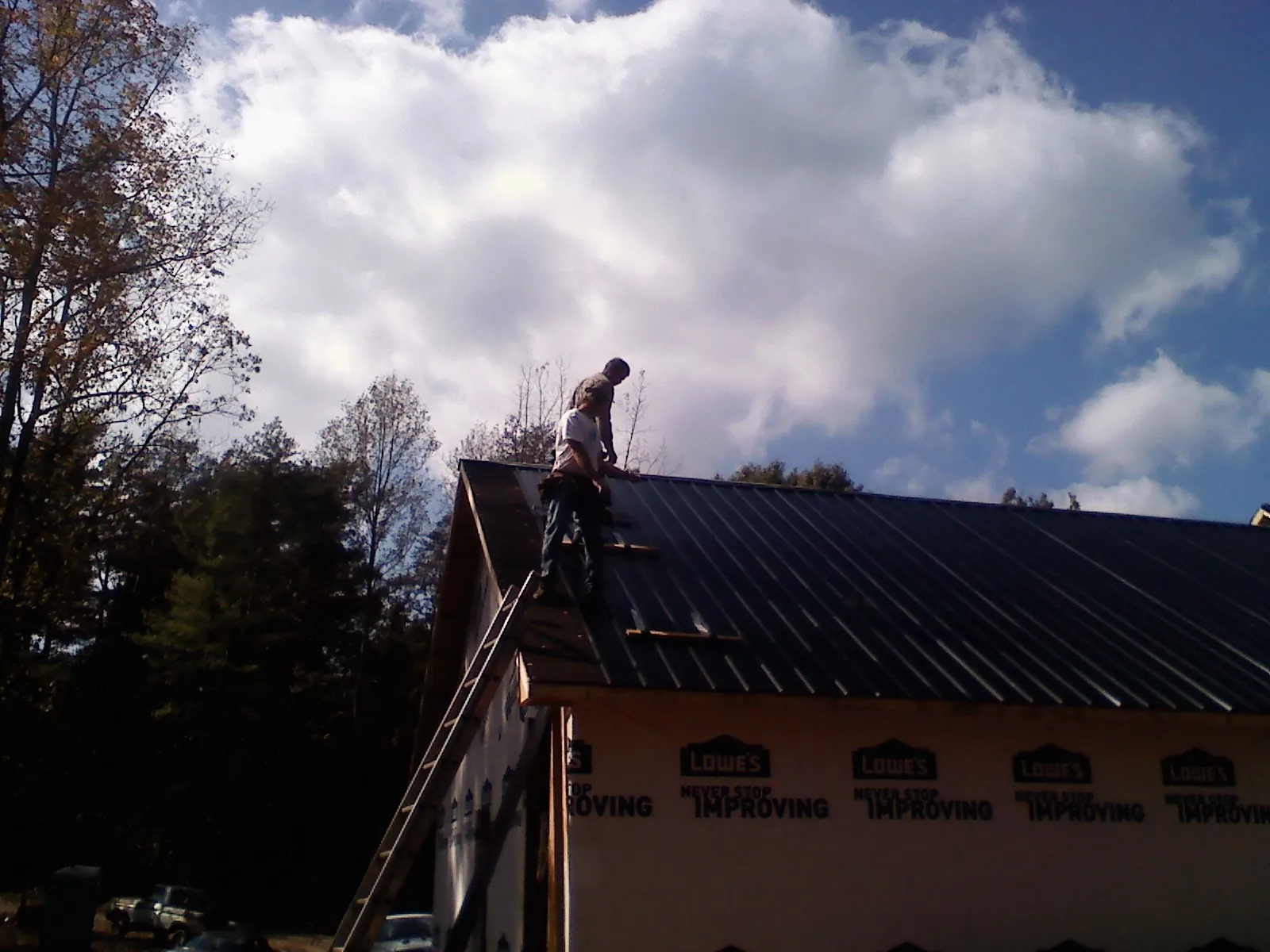 Roofer fastening dark metal panels high against a cloudy sky, from a Roof Inspection job in Bedrock