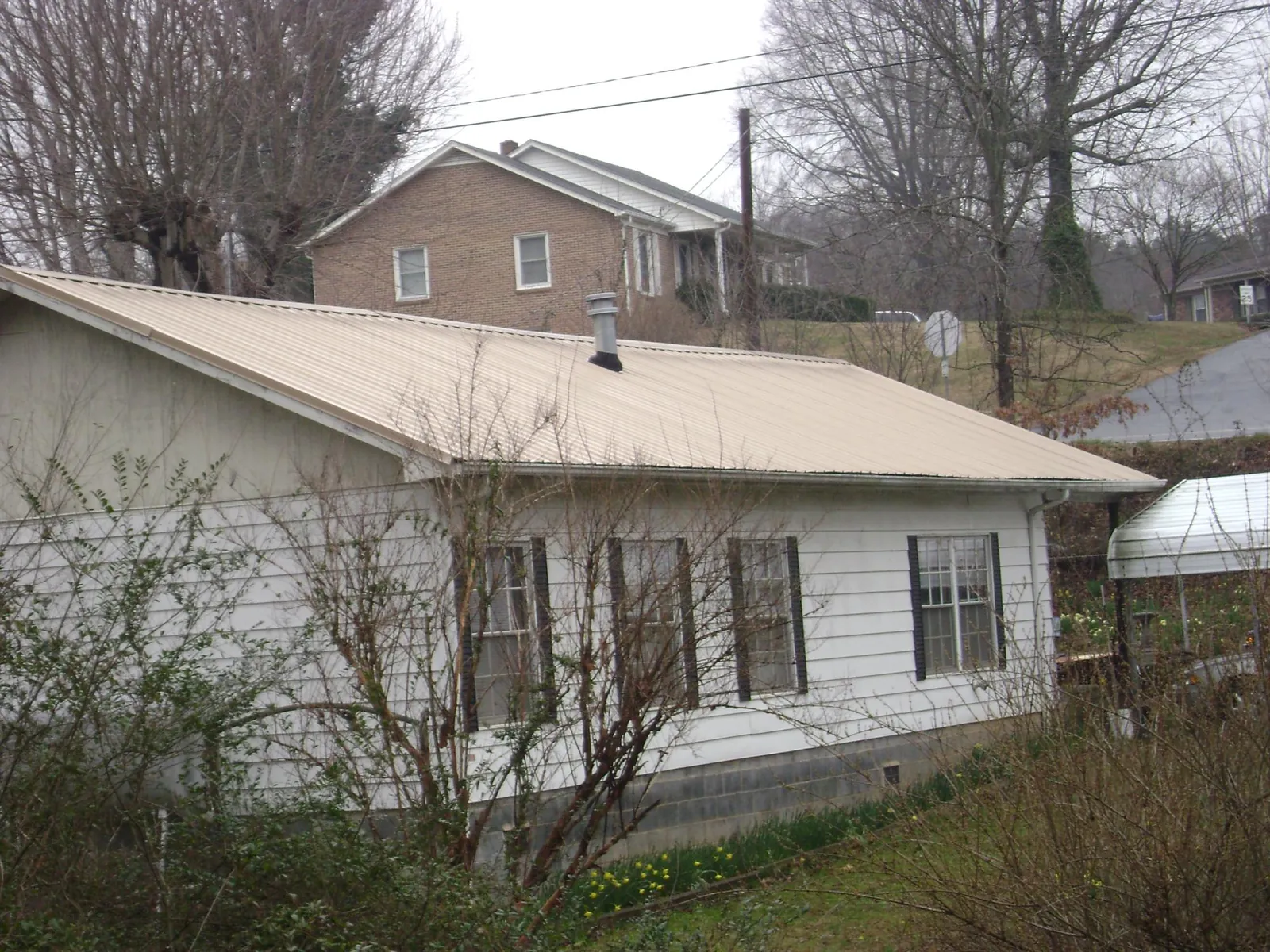 Tan metal roof on a white sided house set into a hillside — Commercial Roofing by Roofing Brothers in Bedrock