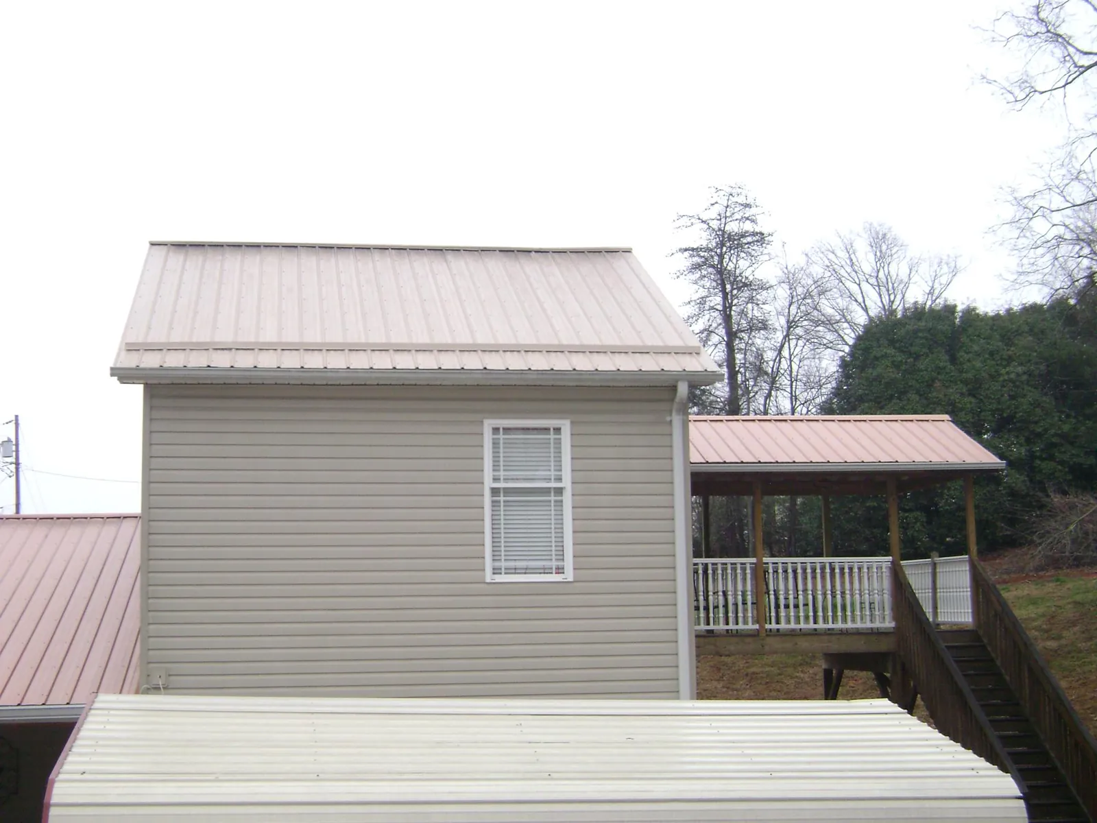 Tan metal roofs on a two story addition and attached porch, from a Roof Replacement job in Bedrock